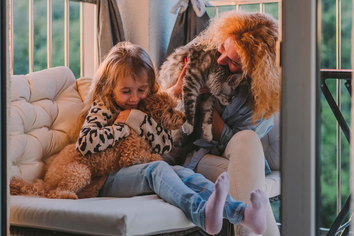 Mum and daughter hugging their dog and cat